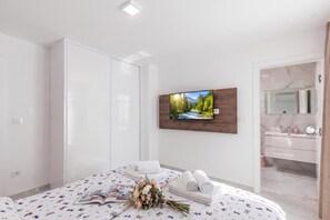 A modern bedroom with a bed, a wall-mounted TV, a bathroom with a mirror, and a door. - Pool Apartments Crikvenica (Crikvenica)