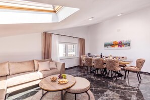 A modern living room with a sofa, a dining table with chairs, and a coffee table with snacks.