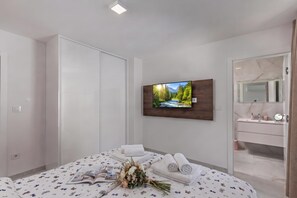 A modern bedroom with a bed, a flat-screen TV, a vanity with a mirror, and a view of a mountain landscape. - Pool Apartments Crikvenica (Crikvenica)