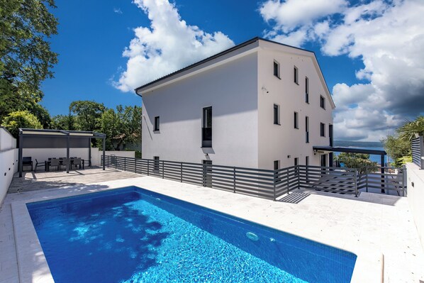 A modern building with a swimming pool, outdoor seating, and a view of the sea. - Pool Apartments Crikvenica (Crikvenica)