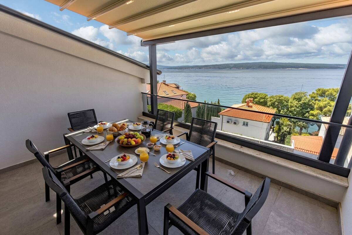 A balcony with a table set for breakfast, overlooking a body of water and distant hills.