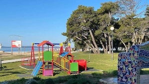 A playground with colorful equipment, a mosaic bench, and a clear view of the beach in the background.