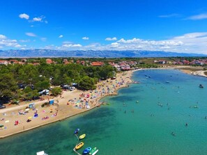 A coastal beach with clear turquoise waters, a sandy shore, and a backdrop of mountains.