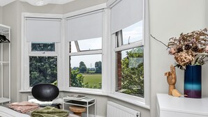 A bedroom with a large bay window, a bed with striped bedding, a wooden floor, and a white desk with a vase of dried flowers. - Unique 2 bedroom Flat in Heart of Walthamstow (Greater London)