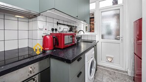 A compact kitchen with a washing machine, a red toaster, and a window with a view of a brick building. - Unique 2 bedroom Flat in Heart of Walthamstow (Greater London)