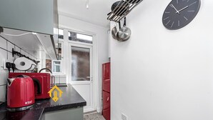 A kitchen with a black countertop, a red kettle, a red refrigerator, and a wall-mounted clock. - Unique 2 bedroom Flat in Heart of Walthamstow (Greater London)