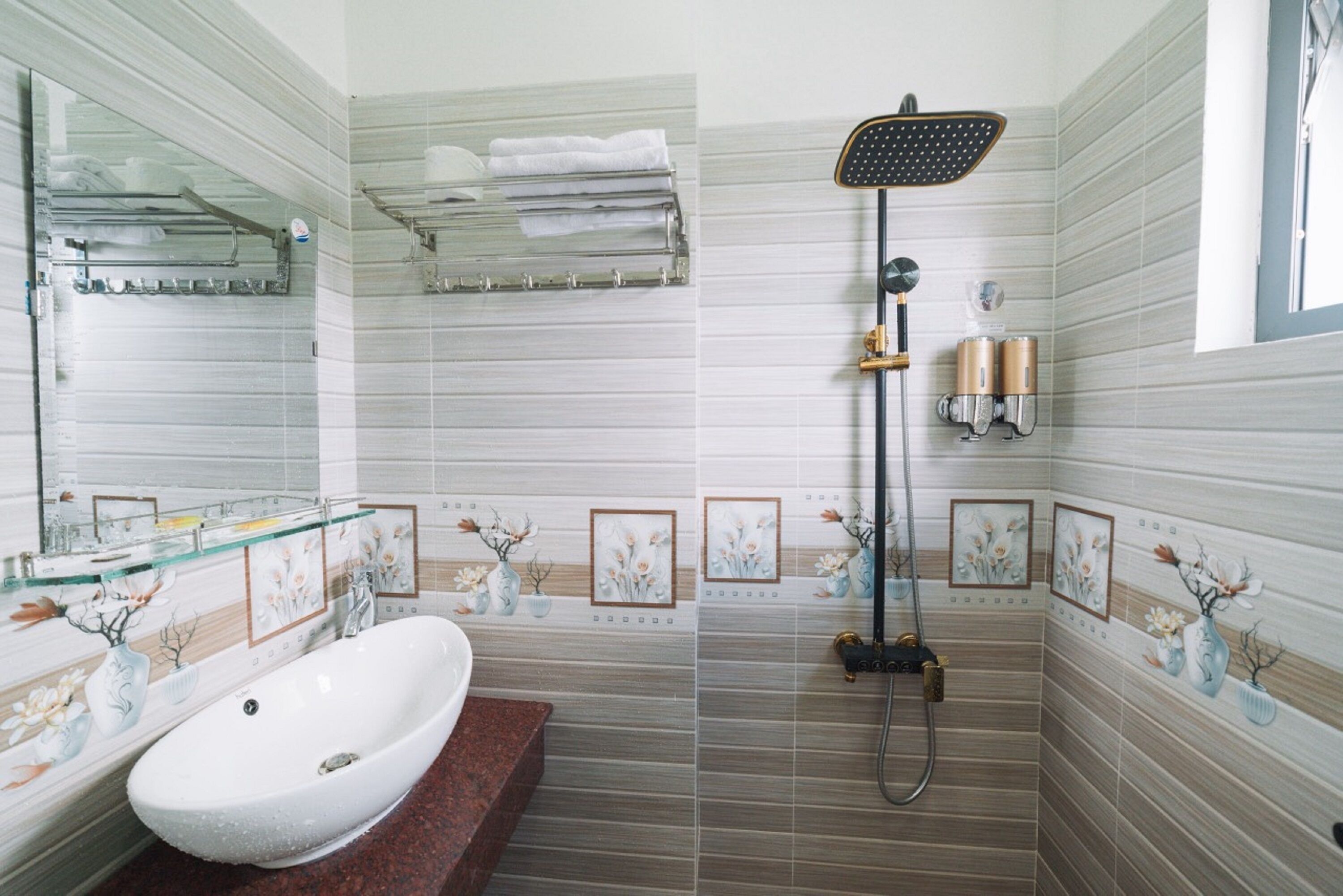 A bathroom with a white sink, a glass shelf, a shower with a handheld showerhead, and decorative floral tiles.