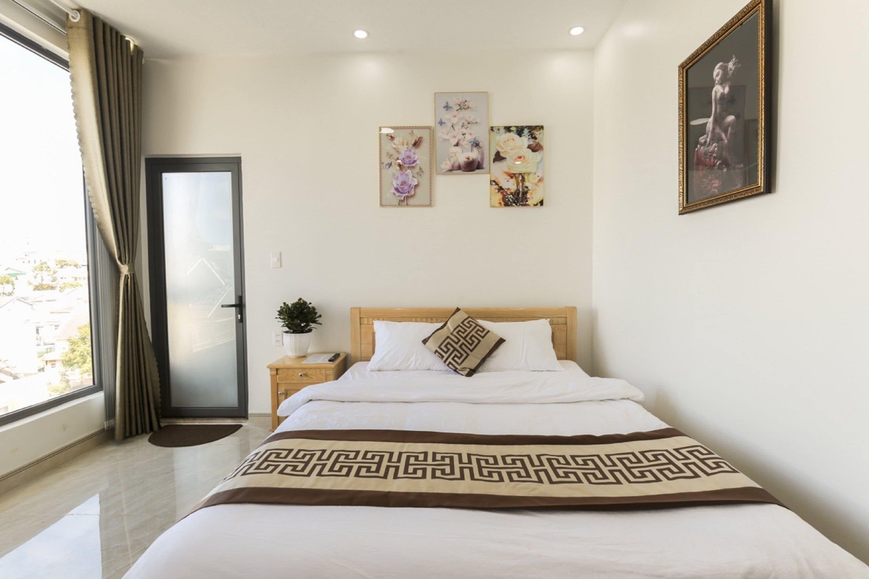 Une chambre d’hôtel avec un lit, une table de chevet, une plante en pot et une fenêtre avec des rideaux.