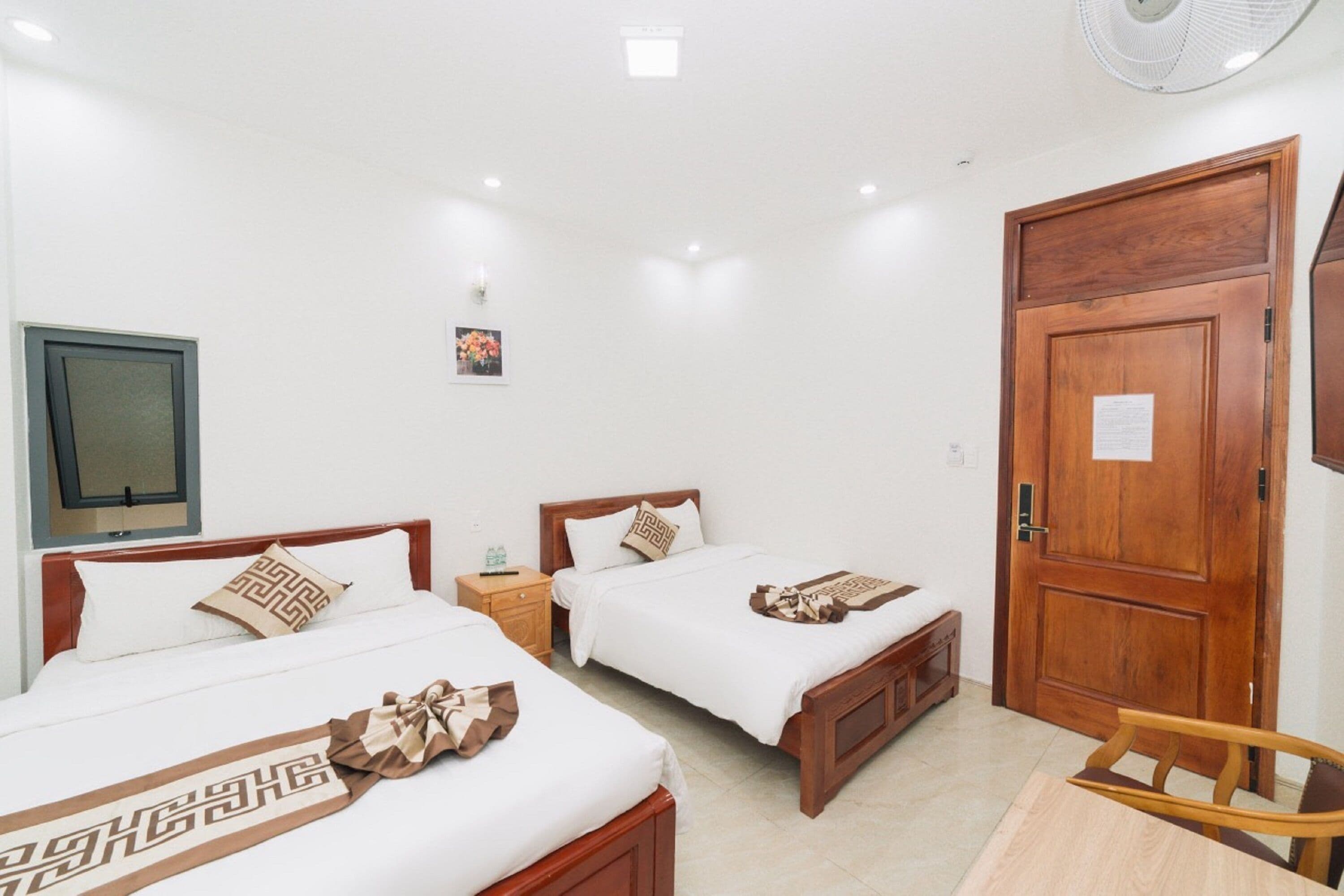 Una habitación de hotel con dos camas, una puerta de madera, una mesita pequeña y una silla.