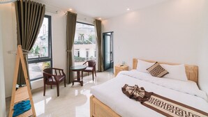 Ein Hotelzimmer mit einem Bett, einem Holzstuhl, einem kleinen Tisch und einem Fenster mit Vorhängen.
