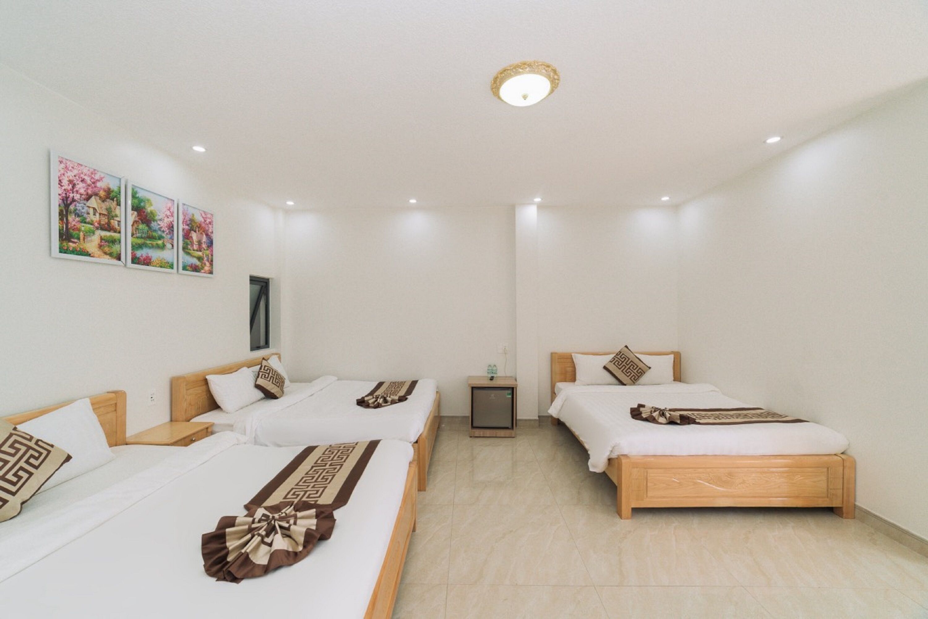 A hotel room with three single beds, a small bedside table with a lamp, and a wall-mounted TV.