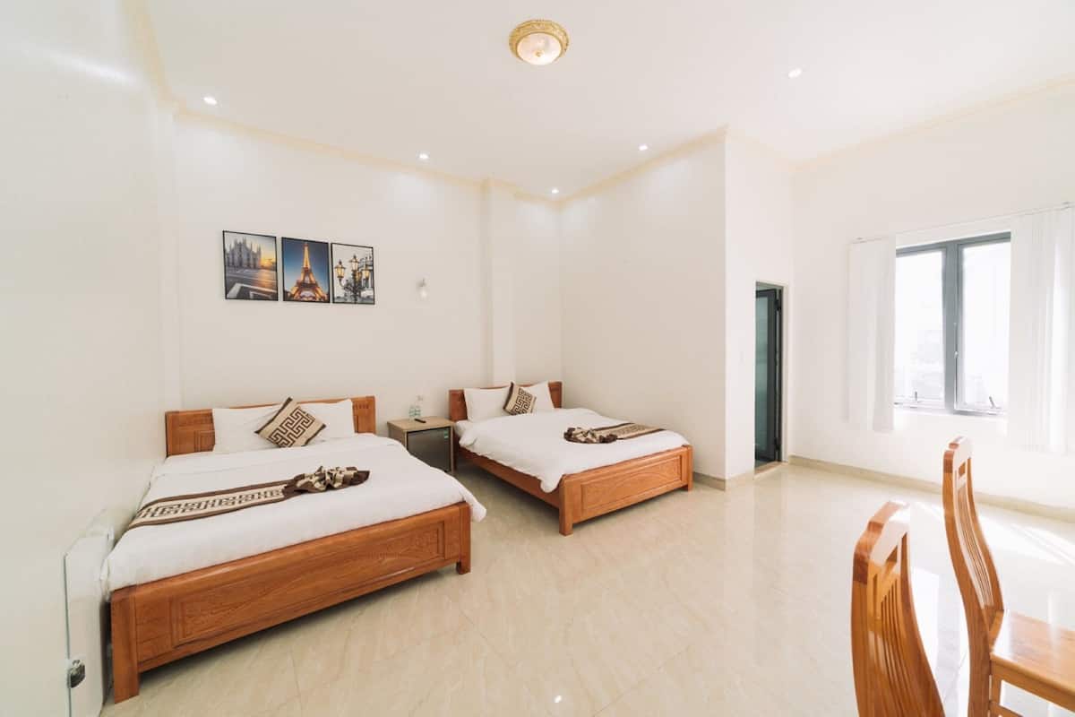 Quarto de hotel com duas camas de madeira, uma mesinha e uma cadeira. Há três quadros na parede.