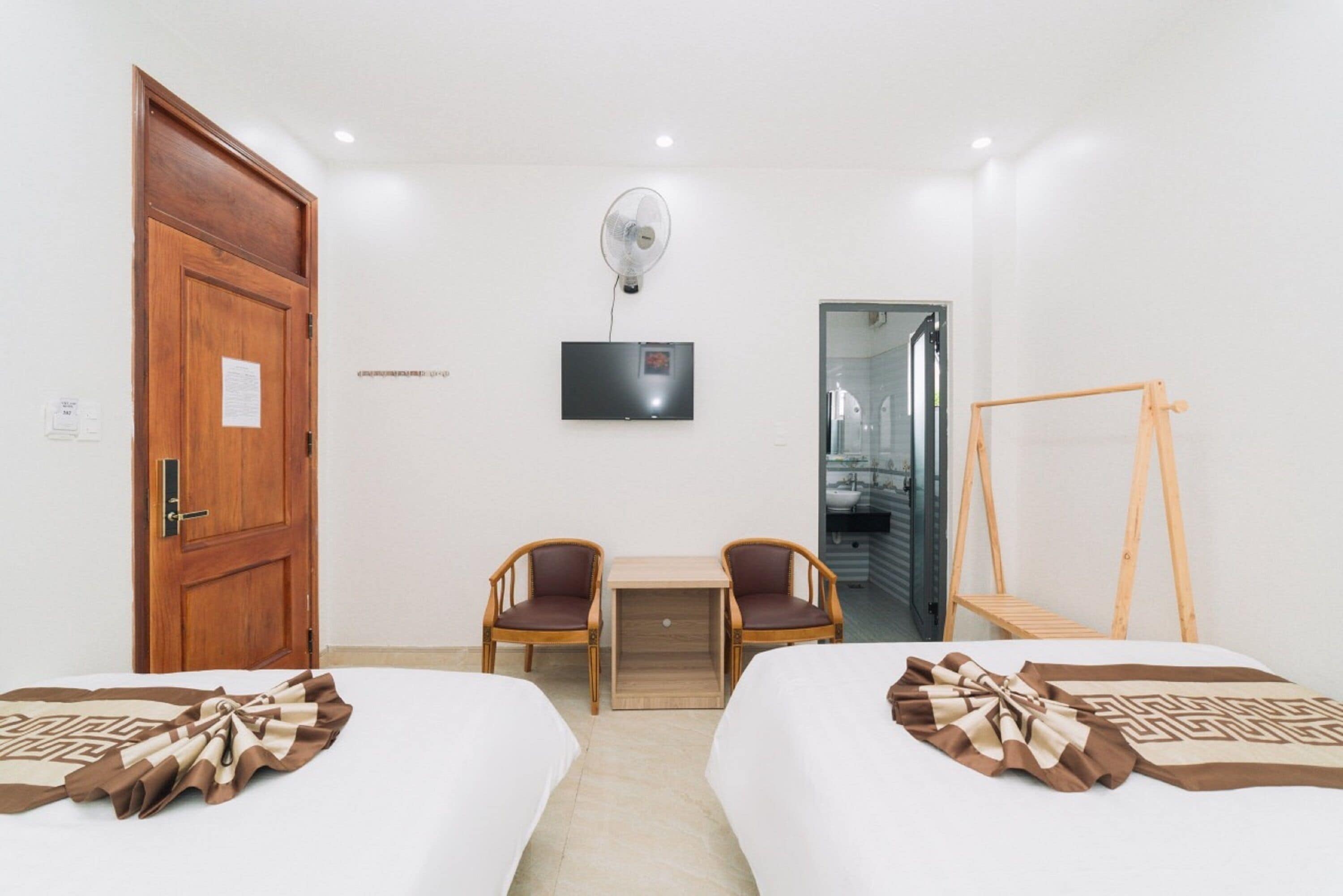 Een hotelkamer met twee bedden, een bureau, twee stoelen, een ventilator, een televisie en een houten schommel.