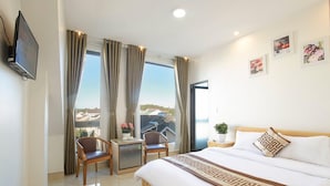 Ein Hotelzimmer mit Bett, Schreibtisch, zwei Stühlen, einem kleinen Tisch, einem Fernseher und einem Balkon mit Vorhängen.