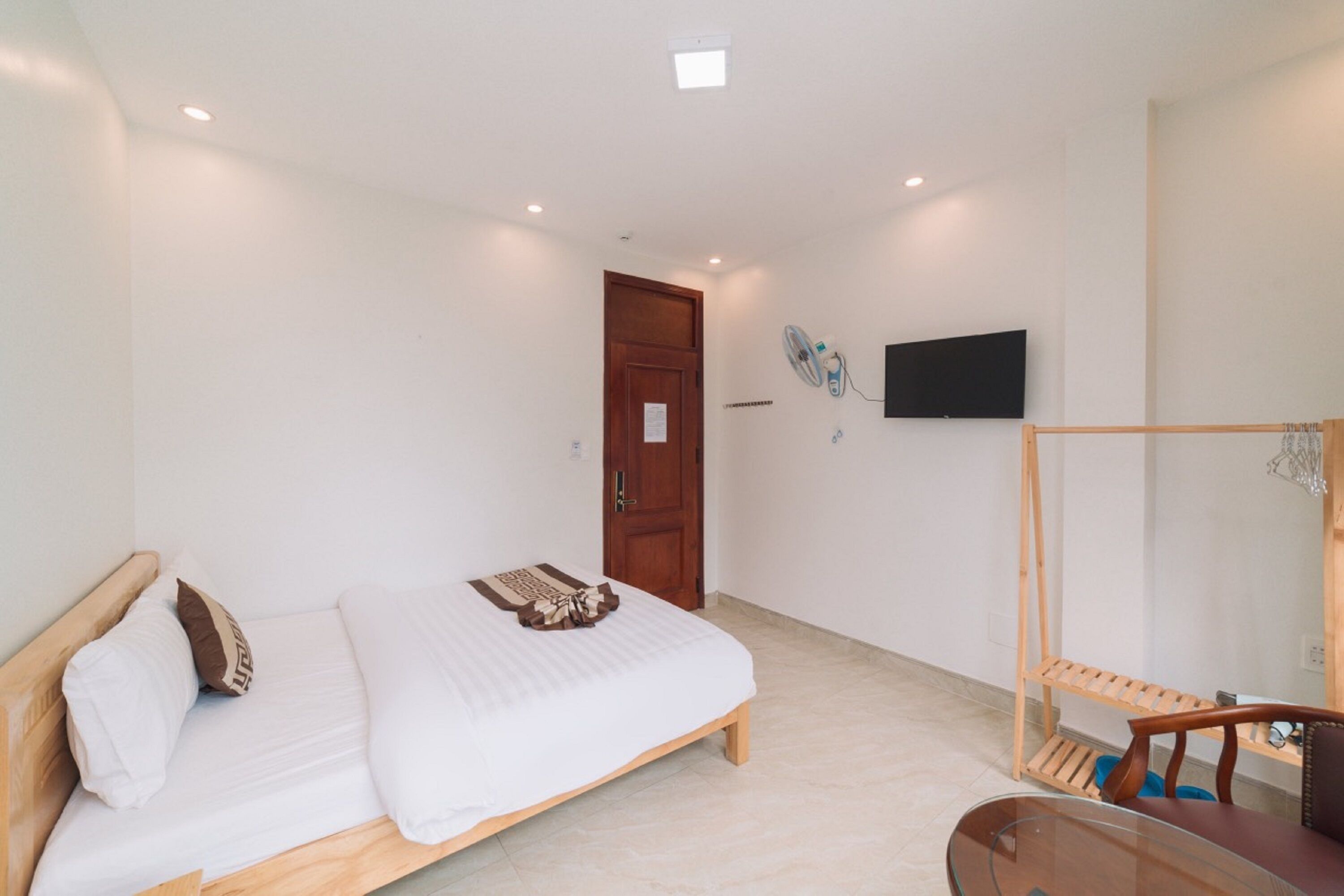 A bedroom with a bed, a wooden chair, a TV mounted on the wall, and a wooden door.