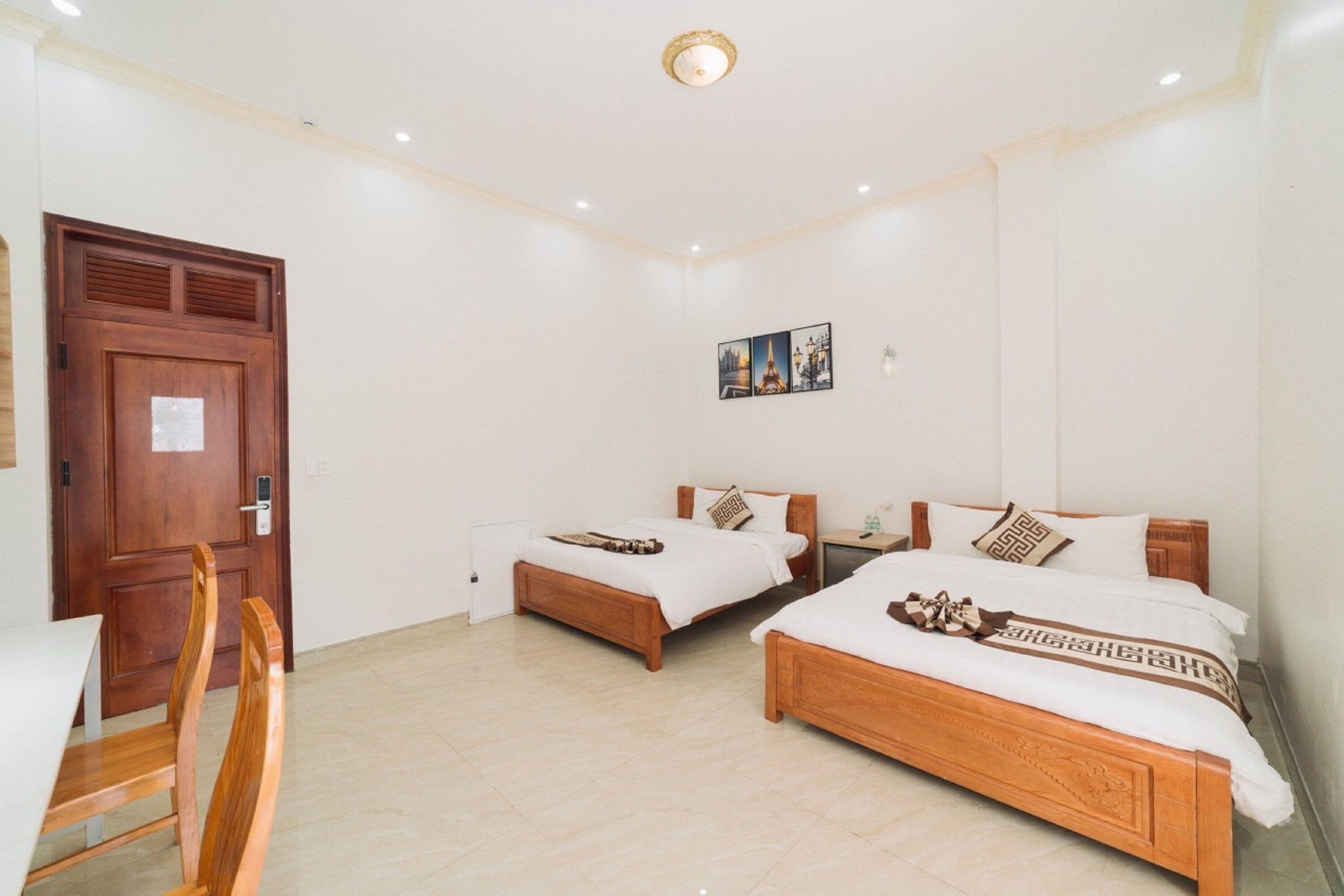 Una habitación de hotel con dos camas de madera, una mesa de comedor con sillas y una puerta.