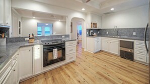 A spacious kitchen with white cabinetry, a large island, a built-in oven, and a dishwasher.