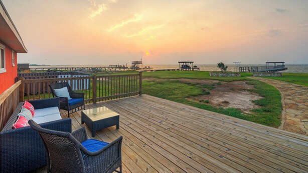 A wooden deck with wicker furniture and a view of the sunset over the water.