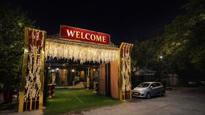 Entrada de hotel con un letrero que dice 'WELCOME', un coche estacionado cerca y un camino bien iluminado que conduce a la entrada.