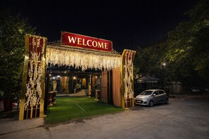 A hotel entrance with a 'WELCOME' sign, a car parked nearby, and a well-lit pathway leading to the entrance. - Hotel Lagoona and Banquet Hall (New Delhi)