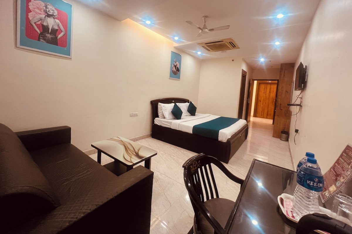 A hotel room with a bed, a desk, a chair, and a couch. There is a ceiling fan and recessed lighting.
