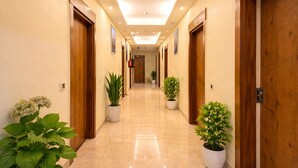 Pasillo de hotel con puertas de madera, plantas en macetas e iluminación empotrada.