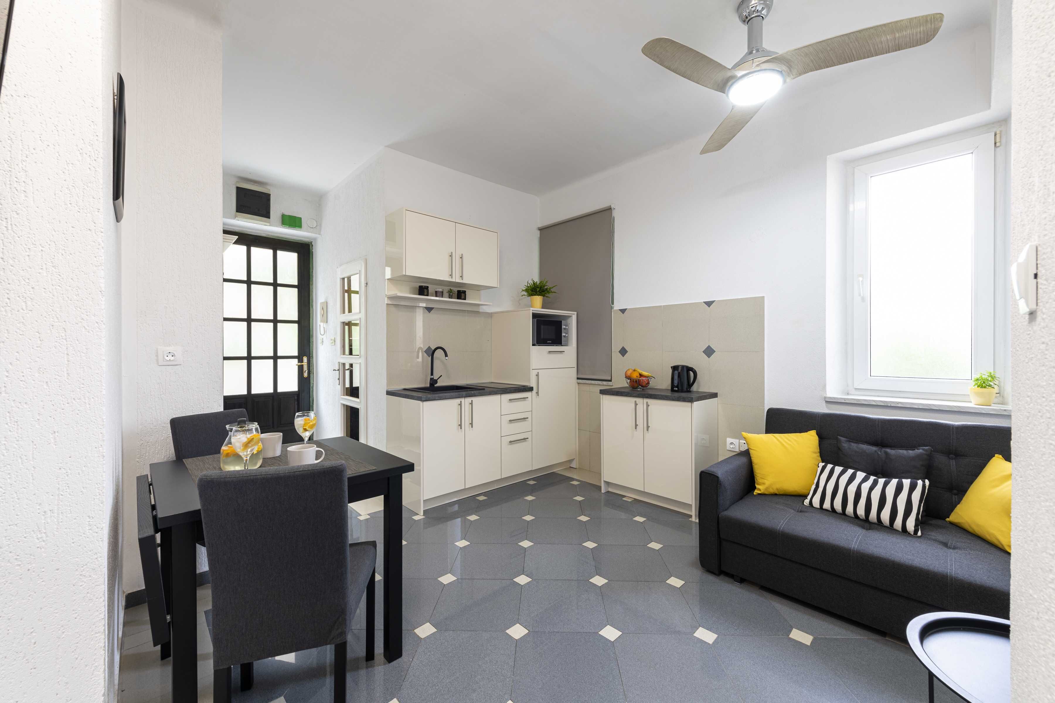 A compact living space with a dining area, kitchenette, and a sofa with cushions.