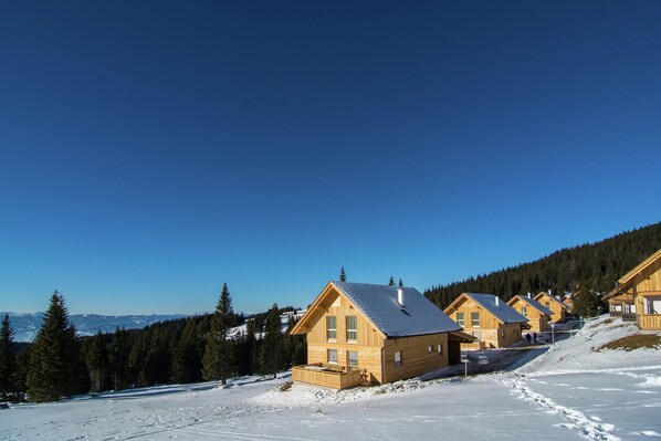 Une rangée de cabanes en bois offrant une vue dégagée sur le paysage enneigé environnant et les montagnes lointaines.