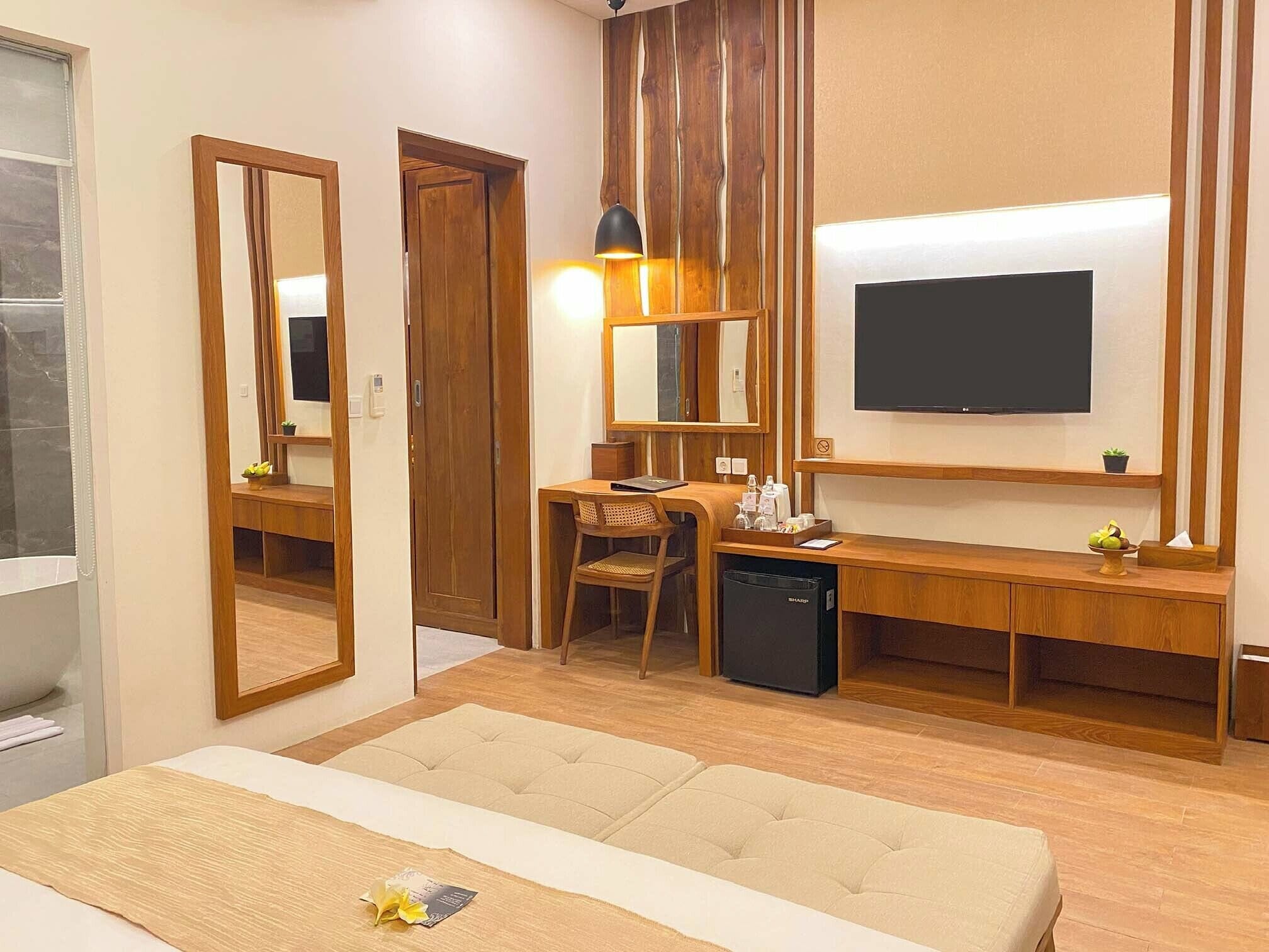 A hotel room with a bed, a desk with a chair, a television, and a mirror.