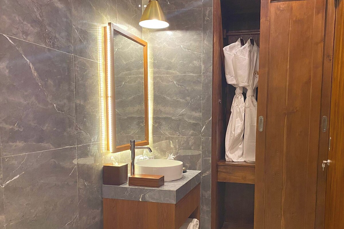 A modern bathroom with a marble wall, a wooden vanity, a freestanding bathtub, and a wooden door closet.