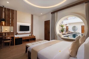 A modern bedroom with a large bed, a desk, a TV, and a view of a pool through a circular window. - The Prime Canggu Bali (Canggu)