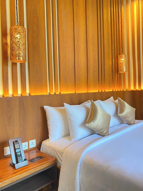 A hotel room with a wooden headboard, a bed with white linens and gold pillows, a bedside table with a phone and remote control, and two hanging lamps with intricate designs.