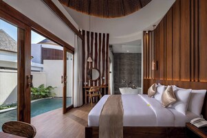 A modern bedroom with a large bed, a bathroom with a bathtub, and a view of a swimming pool.