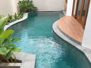 A small, curved swimming pool with clear water, surrounded by plants and a wooden deck. - The Prime Canggu Bali (Canggu)