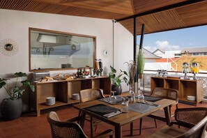 A dining area with a wooden table, chairs, and a large window overlooking a building. - The Prime Canggu Bali (Canggu)