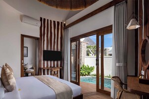 A bedroom with a large bed, a TV, a desk, and a view of a swimming pool.
