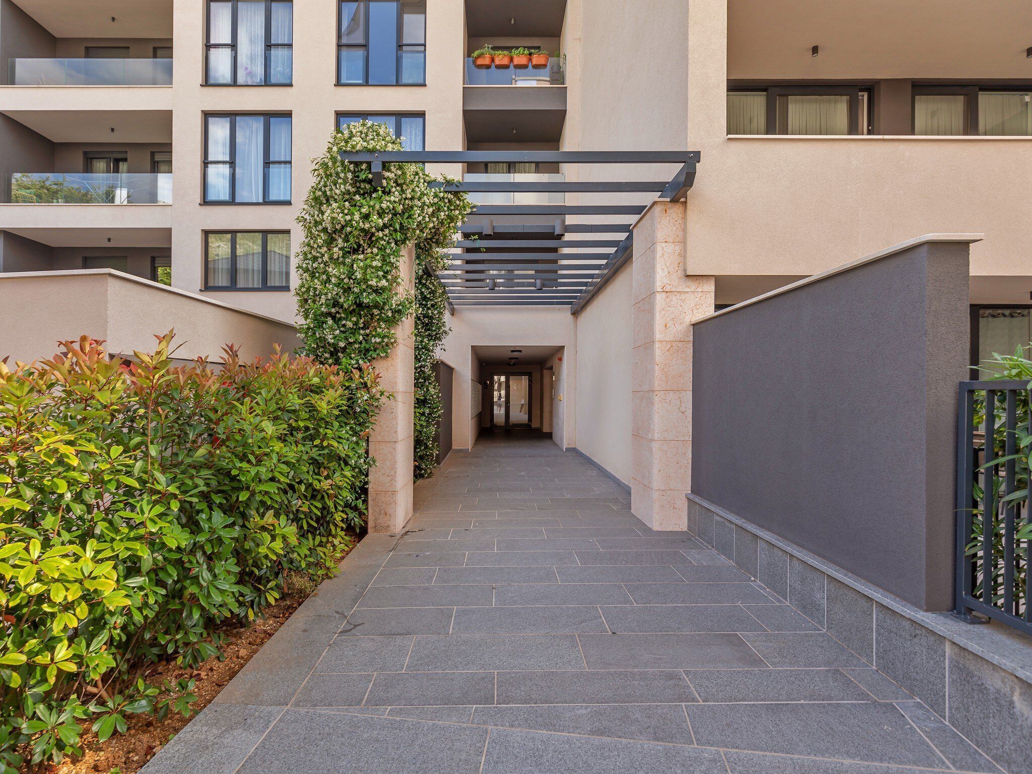 A modern building with a covered walkway, greenery, and a gated entrance.