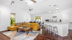 Ein modernes Wohnzimmer mit gelbem Sofa, einem Essbereich und einer Küche mit Barhocker.