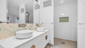 A modern bathroom with two sinks, a large mirror, and a shower area.