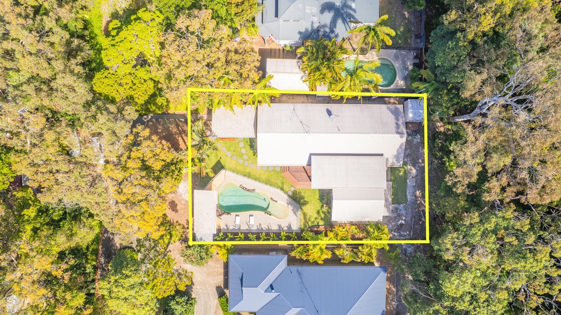 An aerial view of a residential property with a swimming pool, multiple buildings, and surrounding vegetation.