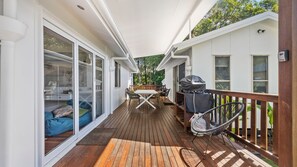 Une terrasse couverte avec une table et des chaises, un barbecue et un fauteuil.