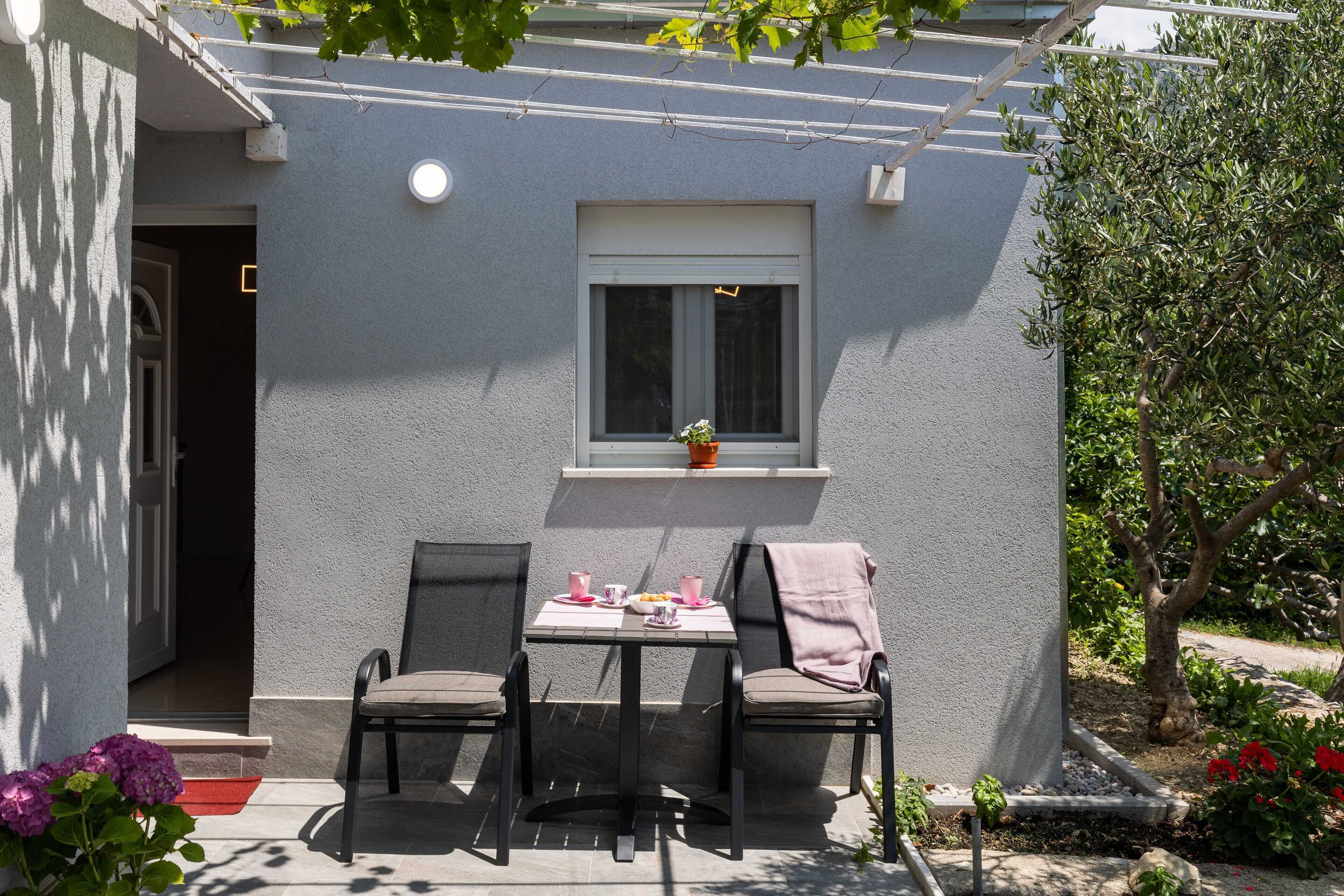 A patio with a table and chairs, a window, and a small plant on the windowsill.