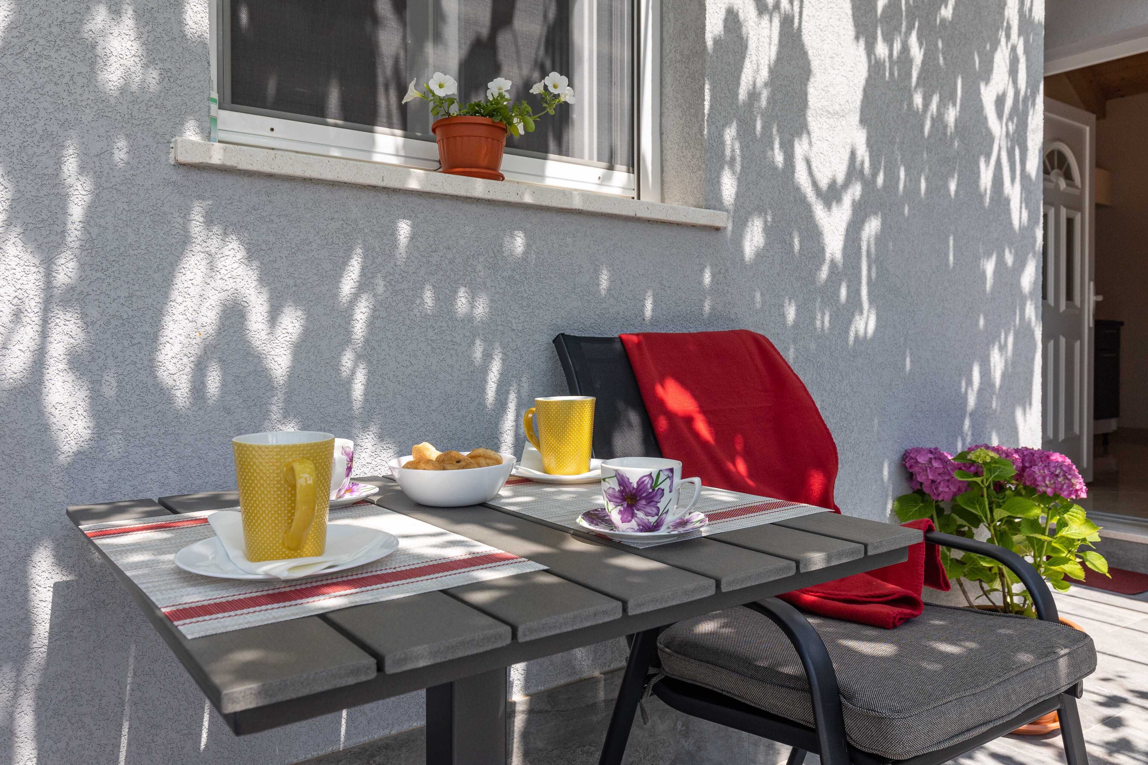 Een terras tafel met een stoel, een schaal lekkernijen en twee kopjes.