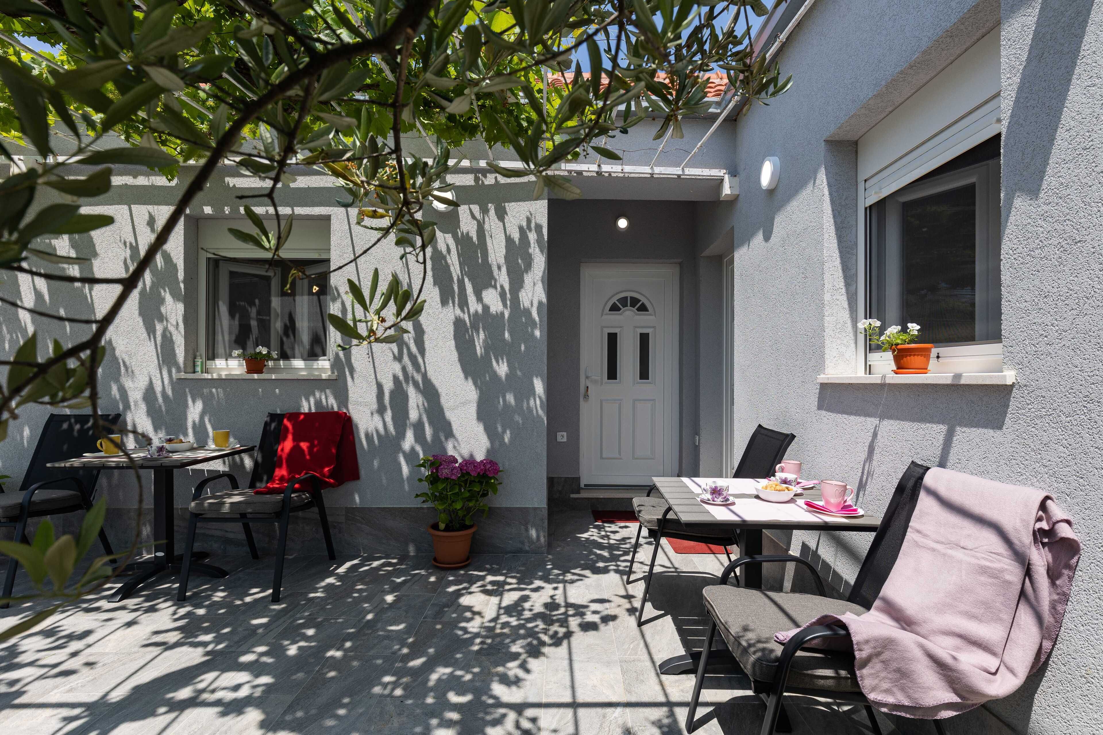 An outdoor patio area with a table and chairs, a potted plant, and a door.