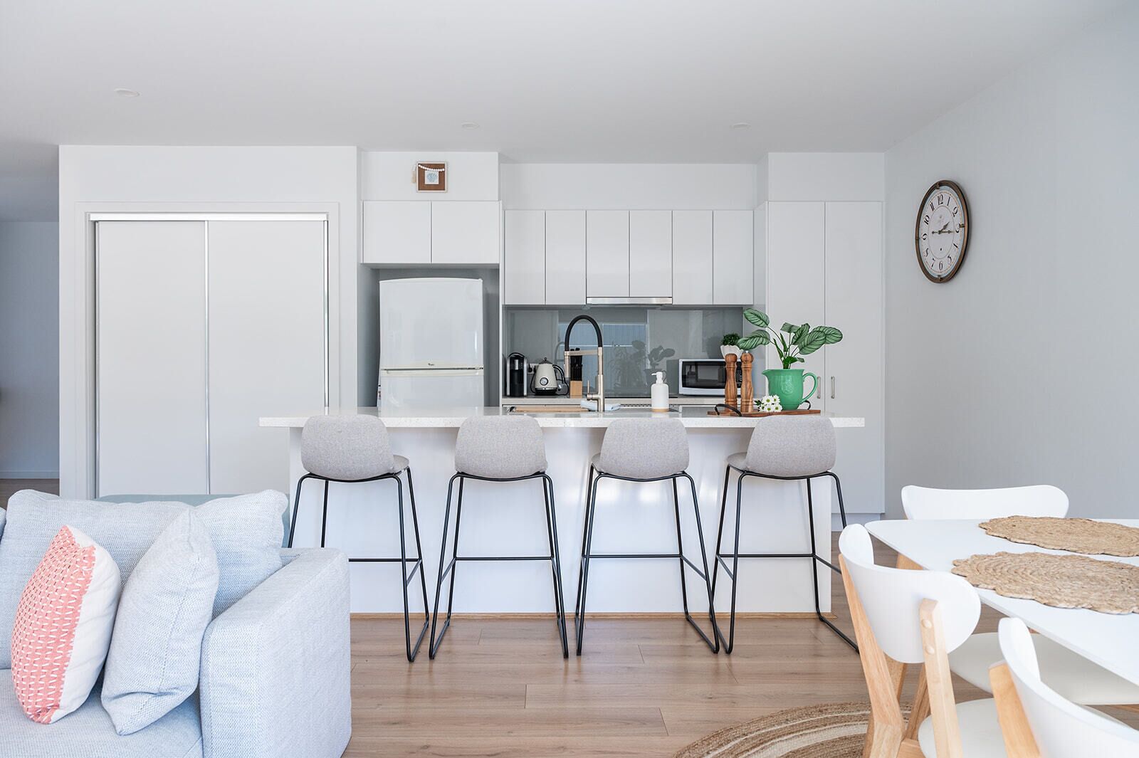 A modern kitchen with white cabinets, a central island with bar stools, a microwave, and a clock on the wall.