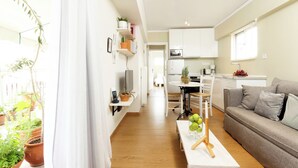 Un appartamento moderno con cucina, zona pranzo e soggiorno. Sono presenti piante in vaso e un divano bianco.