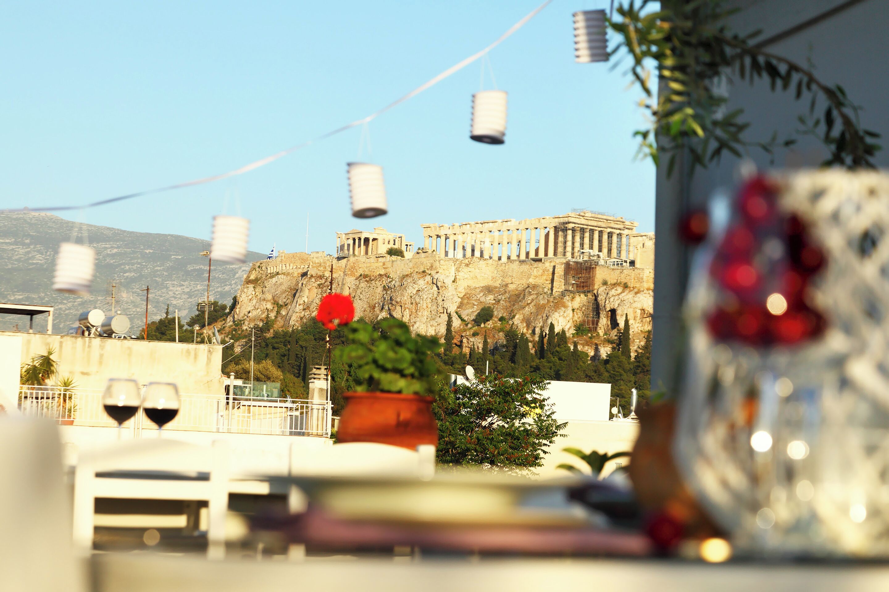 A view of the Acropolis with a table in the foreground featuring a vase and wine glasses.
