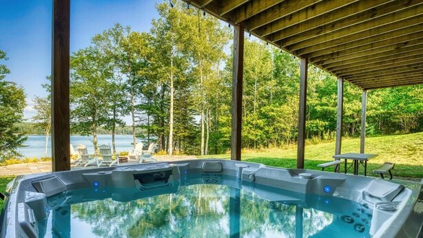 A hot tub with a view of a lake and trees, under a wooden pergola. - Camp Muchemore! Hot Tub, Waterfront! (Hancock)