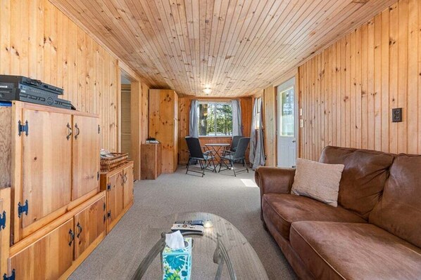 A wooden interior with a brown leather sofa, a dining table with chairs, and wooden cabinets.
