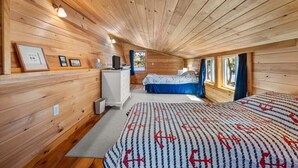 Een blokhutinterieur met houten wanden, een bed met een marine-thema beddegoed, een bureau en een raam.
